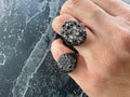 Close-up of a hand wearing two black diamond rings on a dark background
