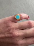Hand wearing a gold ring with a blue gemstone on a gray background