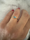 Hand wearing a gold ring with blue enamel on a white background