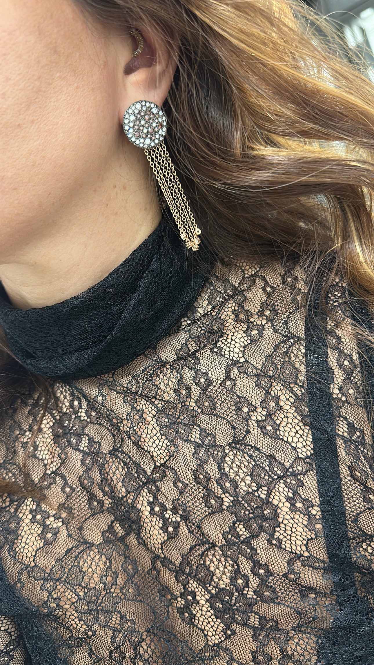 Close-up of a person wearing a lace top and zircon earrings.