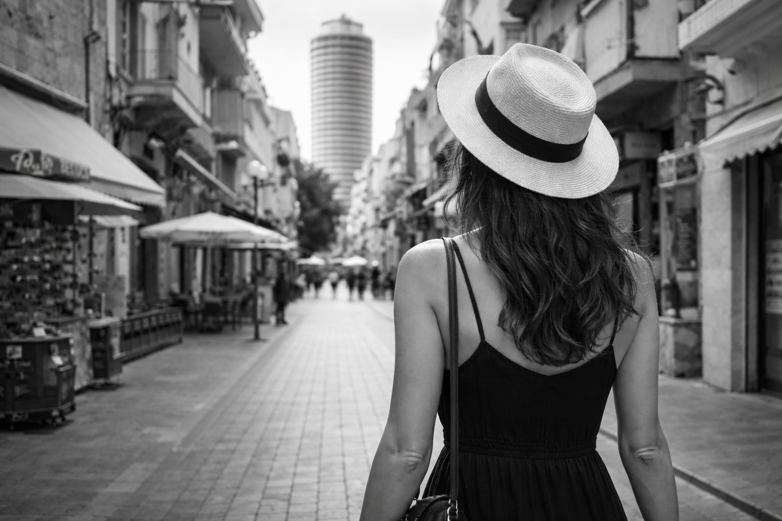 nicole tsiailis in a black dress and white hat walking down a nicosia city street.