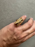 Hand wearing a gold ring with a detailed design on a gray background